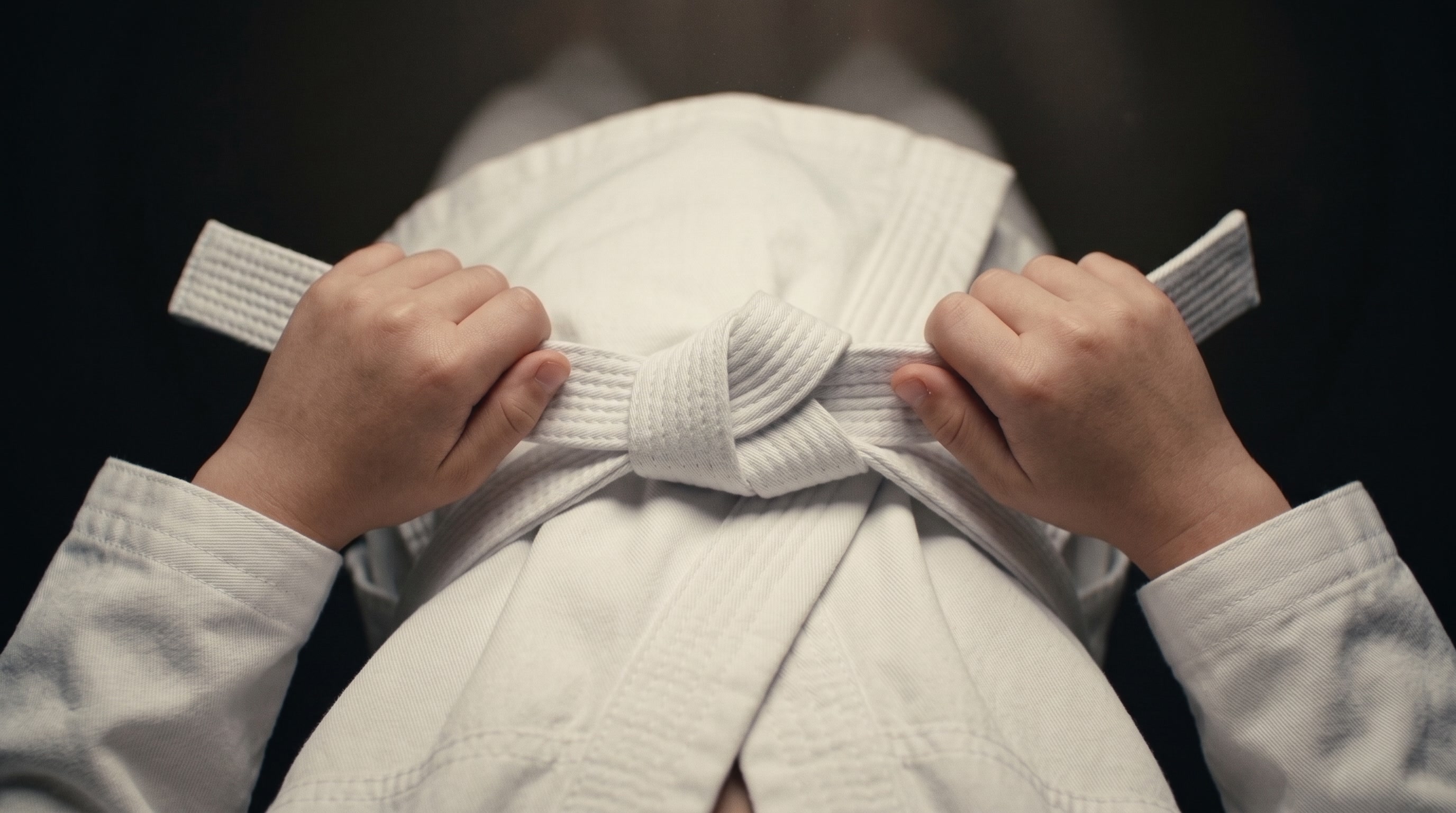 A child's hands tying a new white belt